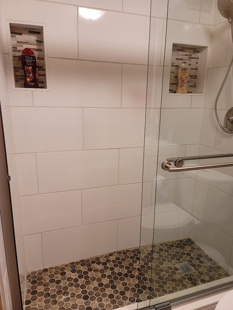 Newly remodeled Master Bathroom with new glistening white tile shower surround and sliding glass doors with adjustable handheld shower head, tile floor, low flow toilet and new vanity.
