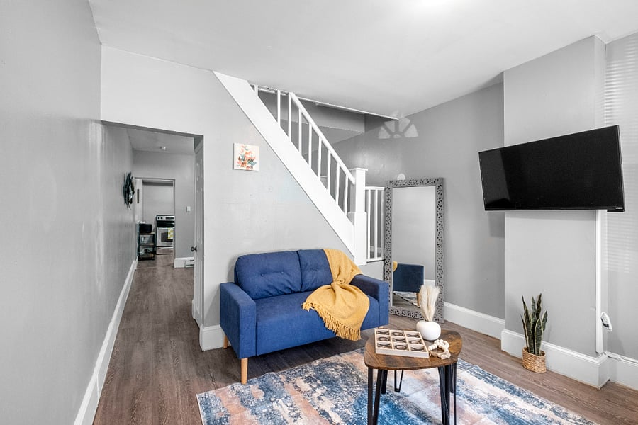 A modern apartment living room with one long sofa, two small sofas, a tea table, and a wall-mounted flatscreen TV offers a stylish and comfortable space designed for both lively gatherings and relaxed entertainment.