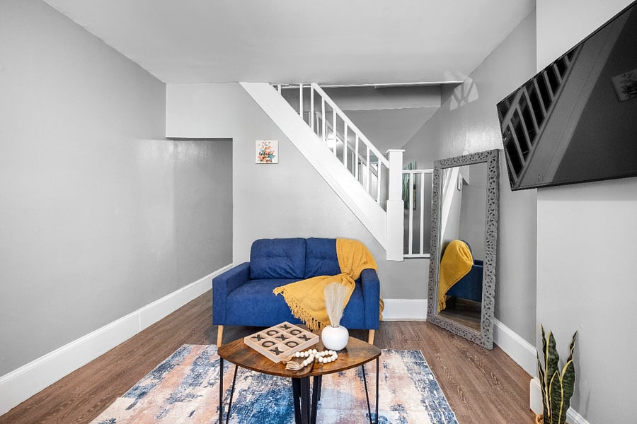 A modern apartment living room with one long sofa, two small sofas, a tea table, and a wall-mounted flatscreen TV offers a stylish and comfortable space designed for both lively gatherings and relaxed entertainment.