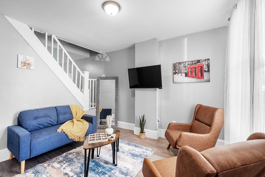 A modern apartment living room with one long sofa, two small sofas, a tea table, and a wall-mounted flatscreen TV offers a stylish and comfortable space designed for both lively gatherings and relaxed entertainment.