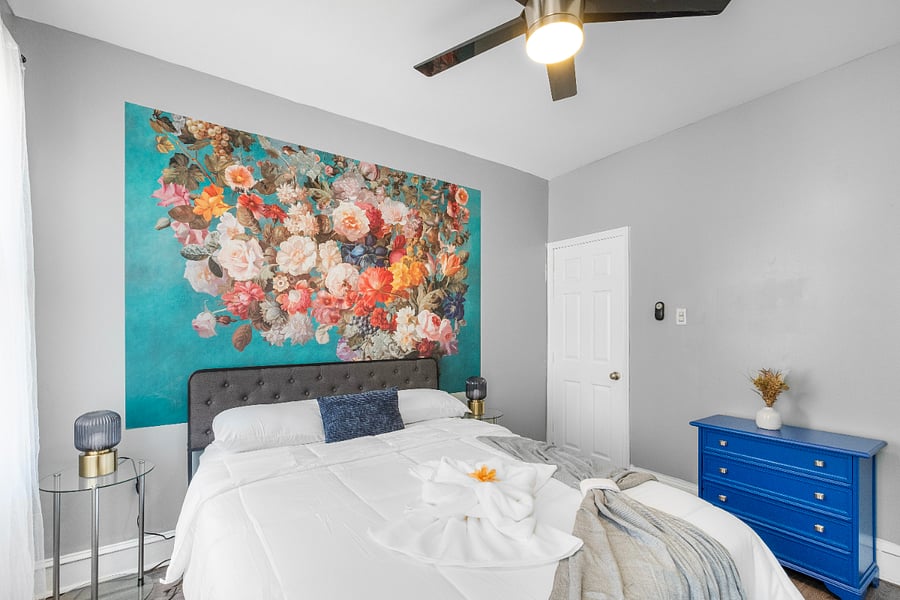 A queen-sized bed in a white bedroom, paired with modern floral wallpaper, creates a crisp and airy space where delicate botanical patterns add a touch of warmth and elegance to the minimalist design.