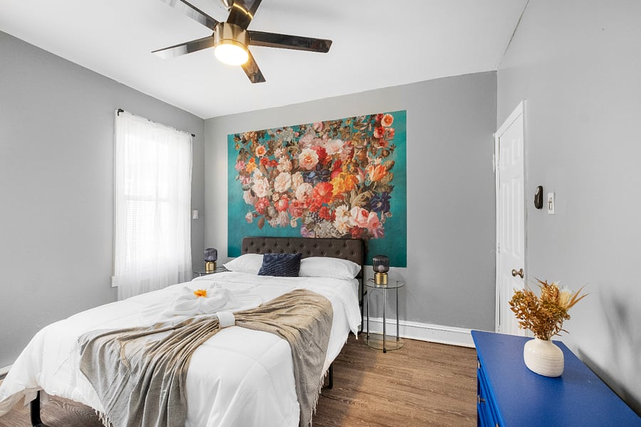 A queen-sized bed in a white bedroom, paired with modern floral wallpaper, creates a crisp and airy space where delicate botanical patterns add a touch of warmth and elegance to the minimalist design.