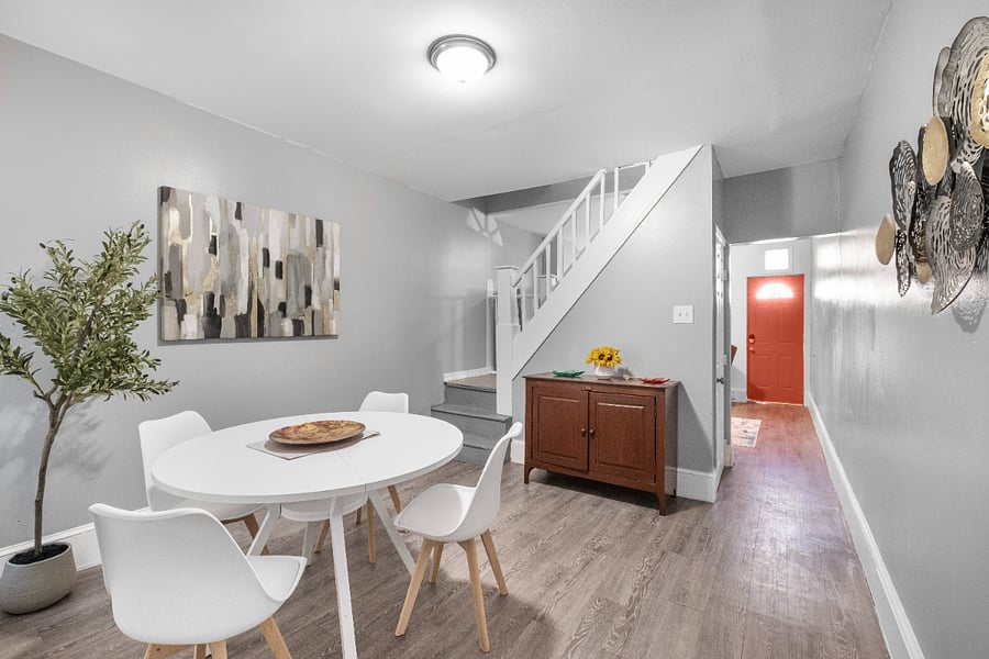 A sleek white dining table positioned beside the staircase is beautifully complemented by a lush green plant, adding a fresh and vibrant touch to the clean, modern space.