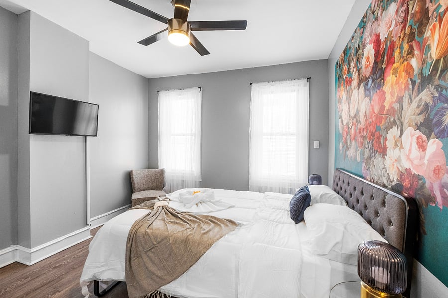 A queen-sized bed in a white bedroom, paired with modern floral wallpaper, creates a crisp and airy space where delicate botanical patterns add a touch of warmth and elegance to the minimalist design.