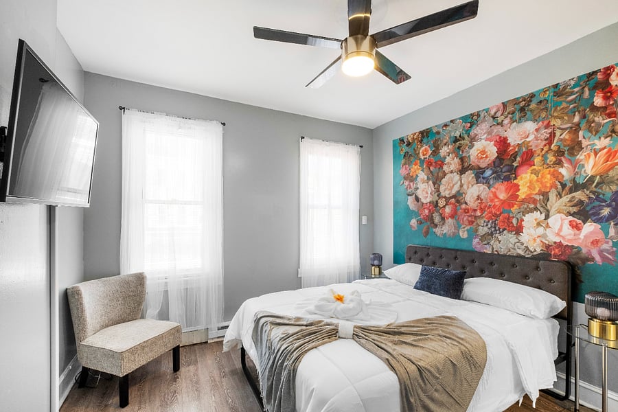 A queen-sized bed in a white bedroom, paired with modern floral wallpaper, creates a crisp and airy space where delicate botanical patterns add a touch of warmth and elegance to the minimalist design.