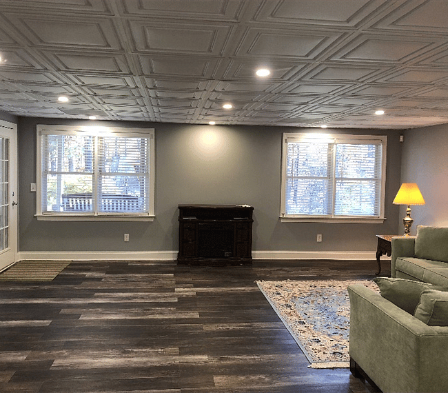 From the back of the living room looking out the windows to the private wooded yard. Entrance door is on the left. Electric fireplace in between the windows.