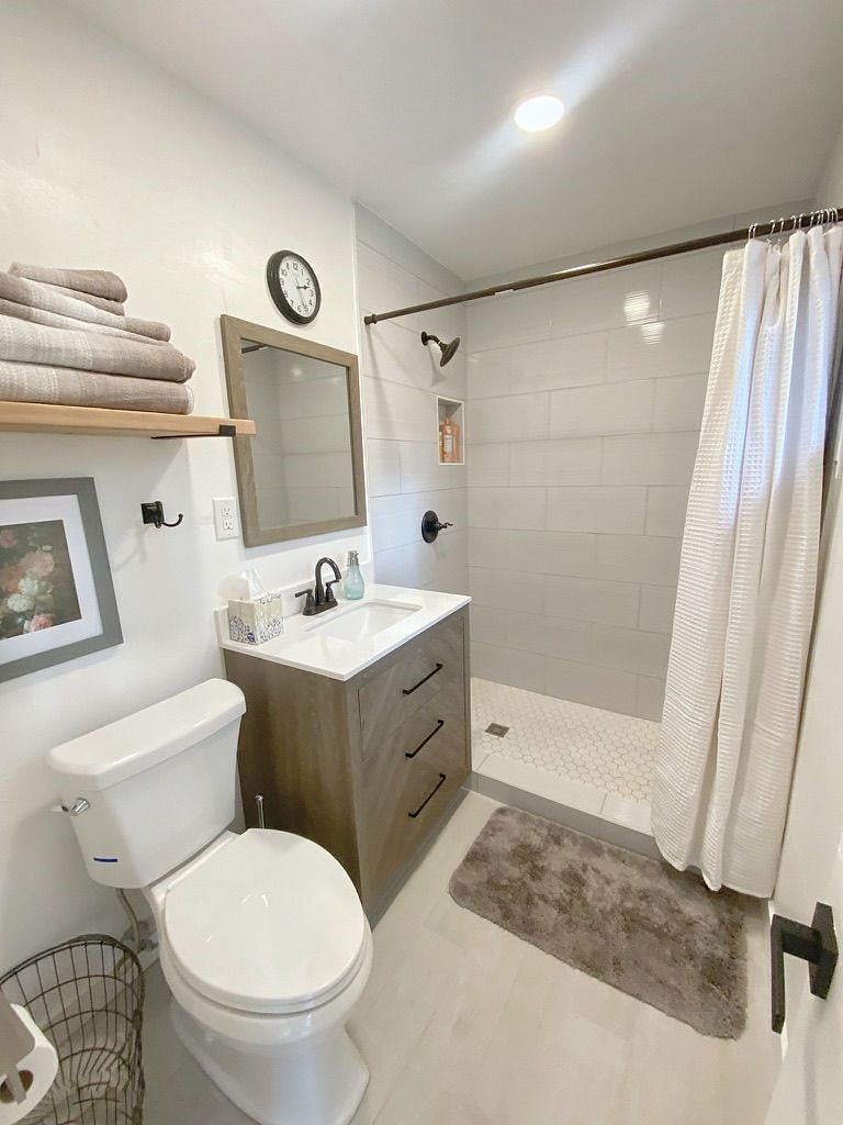 Newly remodeled bathroom has tile shower, vanity, toilet and shelves for towels and toiletries
