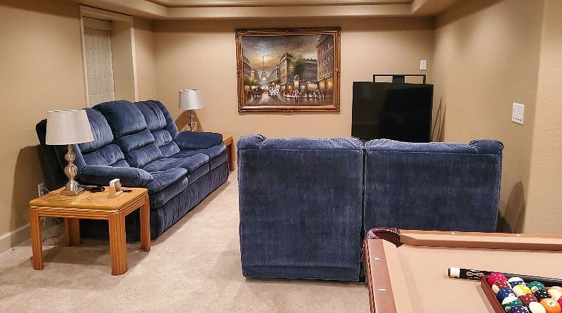 Spacious living area in the basement is furnished with a sofa, loveseat, two end tables, and a corner unit that includes a smart TV for the guests' use.