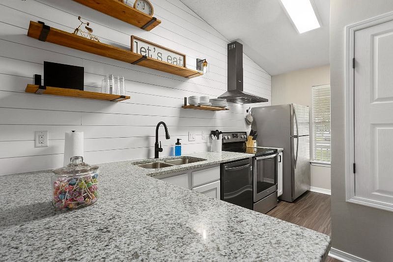 Granite countertop with bar, open shelving and stainless steel appliances