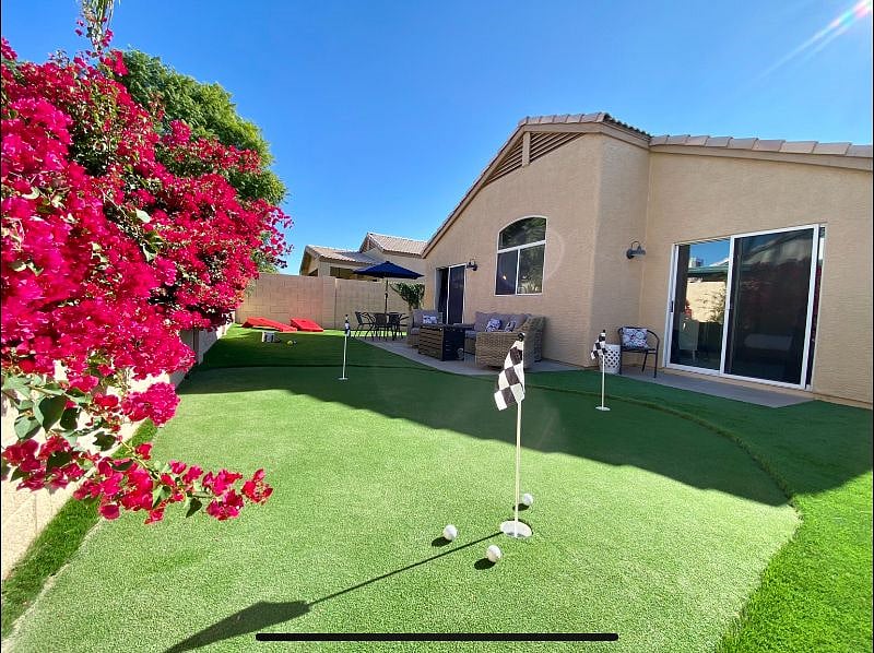 Fully fenced private backyard with putting green, seating with fire-table, and table for outdoor dining.
