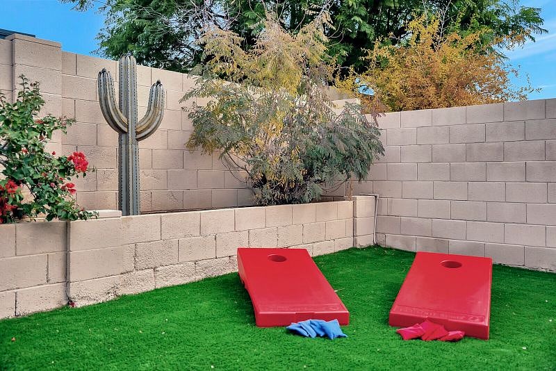 Fully fenced private backyard with putting green, seating with firetable, and table for outdoor dining.