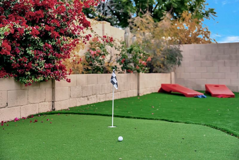 Fully fenced private backyard with putting green, seating with firetable, and table for outdoor dining.