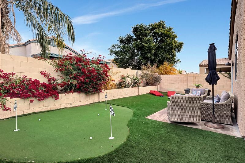 Fully fenced private backyard with putting green, seating with firetable, and table for outdoor dining.