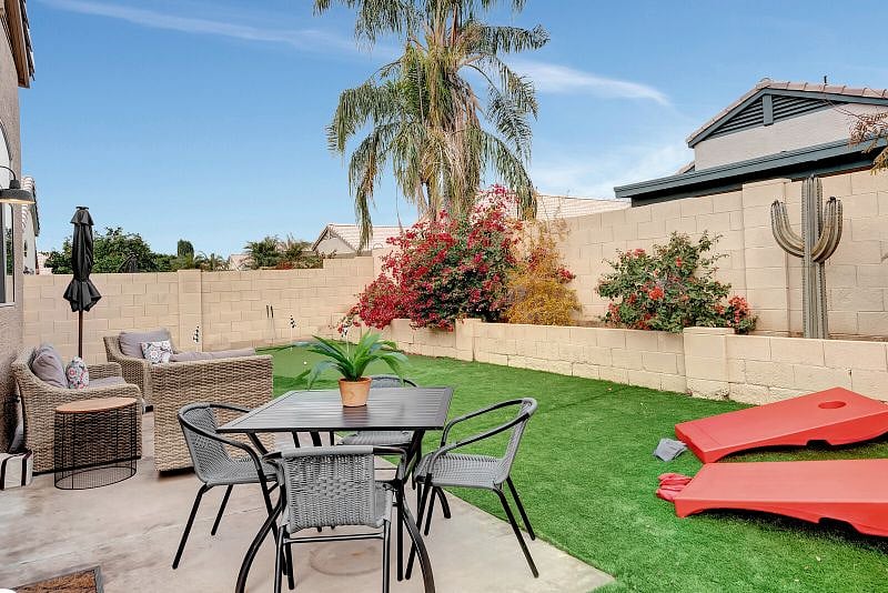 Fully fenced private backyard with putting green, seating with firetable, and table for outdoor dining.