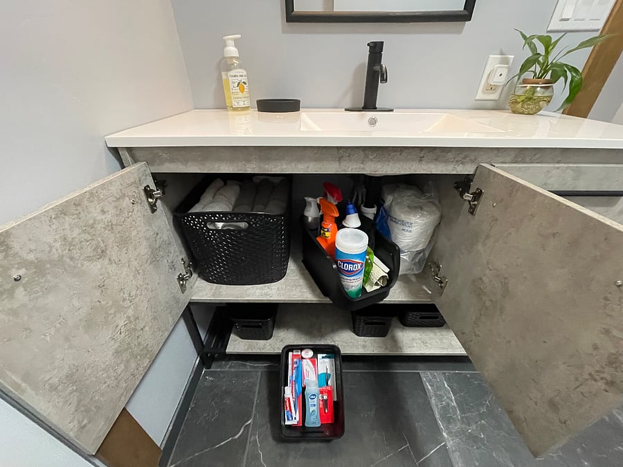 Bathroom vanity is stocked with extra towels, cleaning supplies, starter items, and baskets for individual storage. 