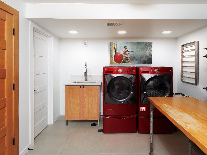 Laundry room provided, including modern front-load washer/dryer, ironing board/iron, and an oversize folding table