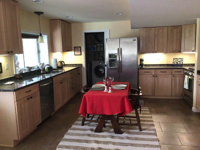 At the other end of the room is a full kitchen with granite countertops. Beyond the door is a utility room with a combination washer and dryer. The windows look on onto a large backyard.