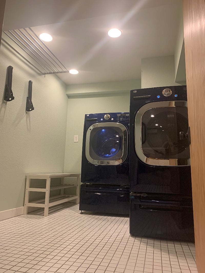 Private laundry room/mud room with tiled floor, foldable bike rack bars, air dryer rack, 2 hampers, full-size ironing board + new iron, large-capacity front-load washer and dryer.