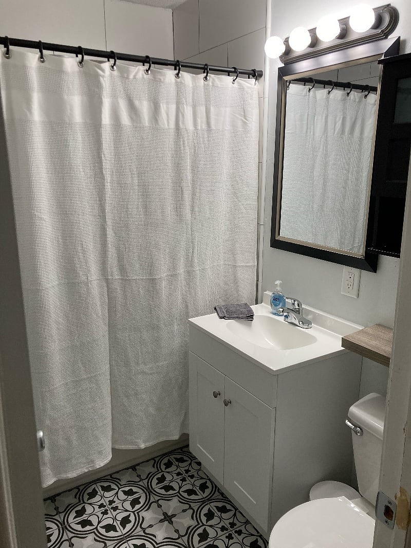 Updated bathroom with black & white tiling, towels, and cleaning supplies.