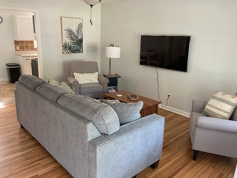 Living area with couch, accent chairs, smart TV, and newly refinished hardwood floors.