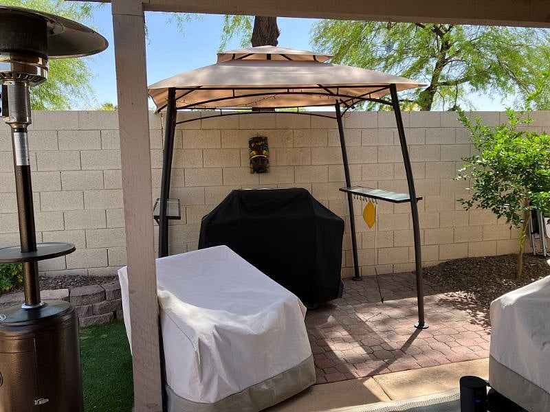 Covered Weber gas grill just outside of a covered patio with seating for 4