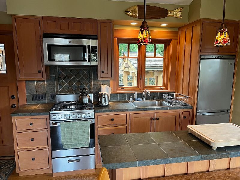 Kitchen with island for prepping + gas cooktop & oven + coffee maker, toaster, fridge/freezer, along with pots and pans, utensils and dishes.