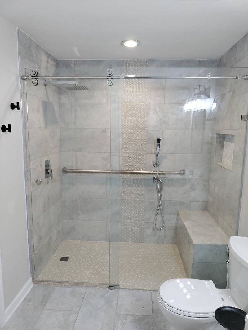 Tile floor to ceiling, barrier-free shower with bench, rain shower head, sprayer and handrail.