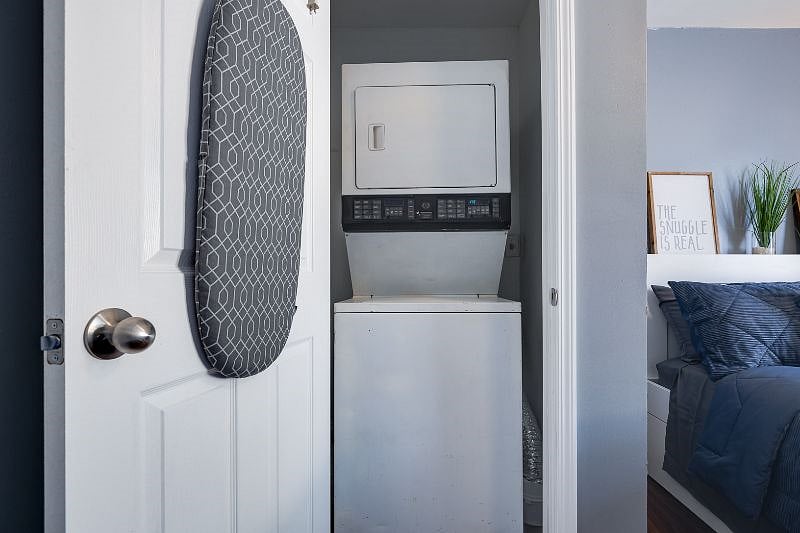 Laundry closet with stackable washer/dryer. Ironing board and iron hang in the caddy of this closet door. 