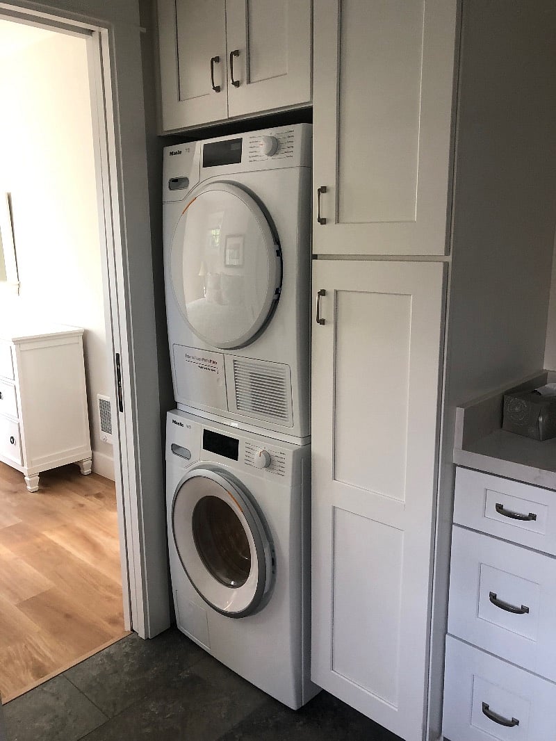 Miele washer and ventless dryer in bathroom. storage cabinets and large vanity.