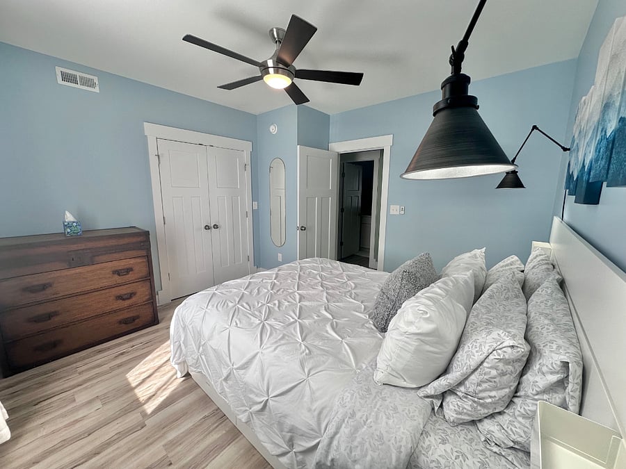 The bedroom features a queen-size bed, chest of drawers, closet with overhead light, and a full-length mirror. 6 slow close action drawers on the bed frame provide additional storage under the bed.