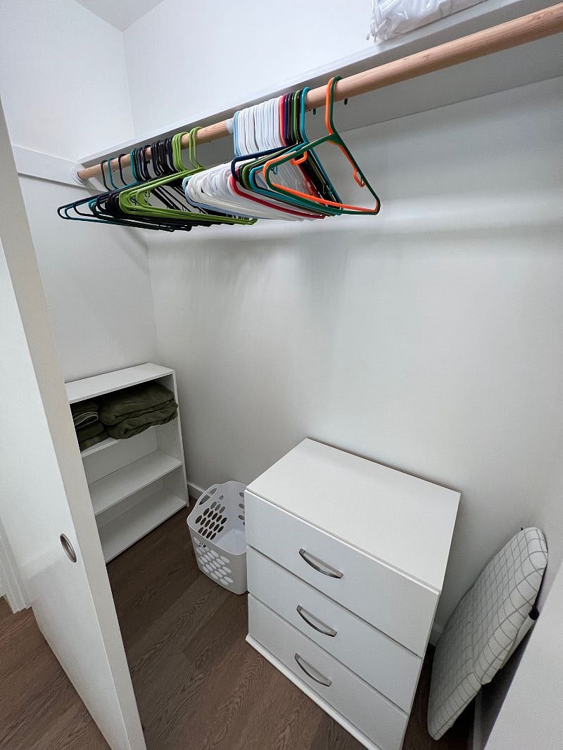 Closet with 3-drawer dresser, shelves, laundry basket, hangers, iron and ironing board