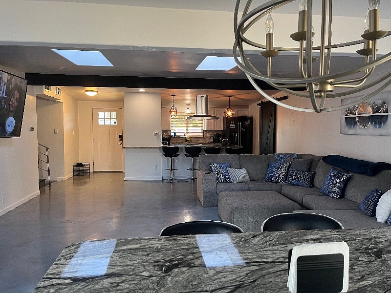 View of large, open living space from behind dining table. Check out the 75-inch smart tv with voice control, sound bar, and speakers. 