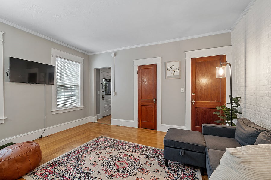 Cozy first-floor living room with a plush couch, accent chair, bar cart, and TV. A perfect spot to relax, watch your favorite shows, or enjoy a quiet evening in this comfortable, welcoming space.