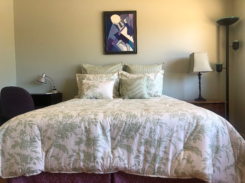 Queen bed with sage green cotton linens, night stand and desk/chair