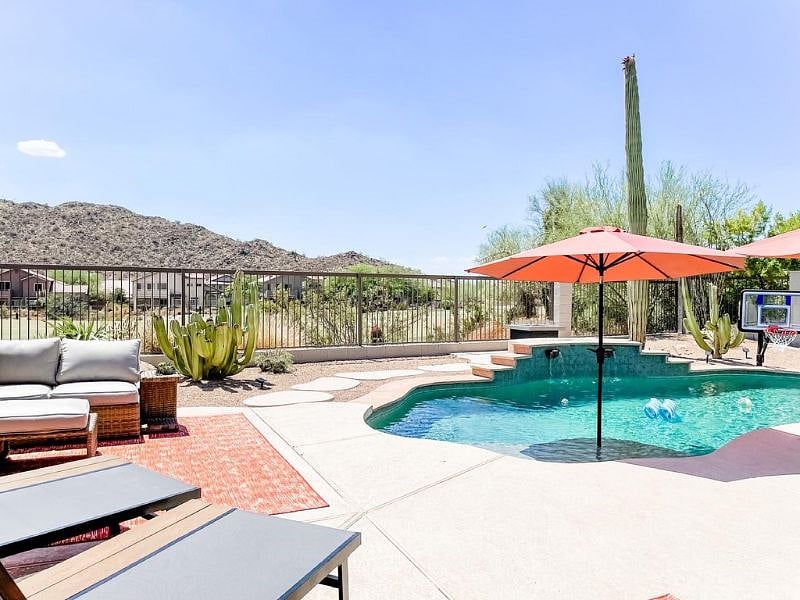 Backyard equipped with 4 lounge chairs, two swivel chairs, bar cart, outdoor sectional, propane firepit, outdoor gas BBQ and umbrellas.