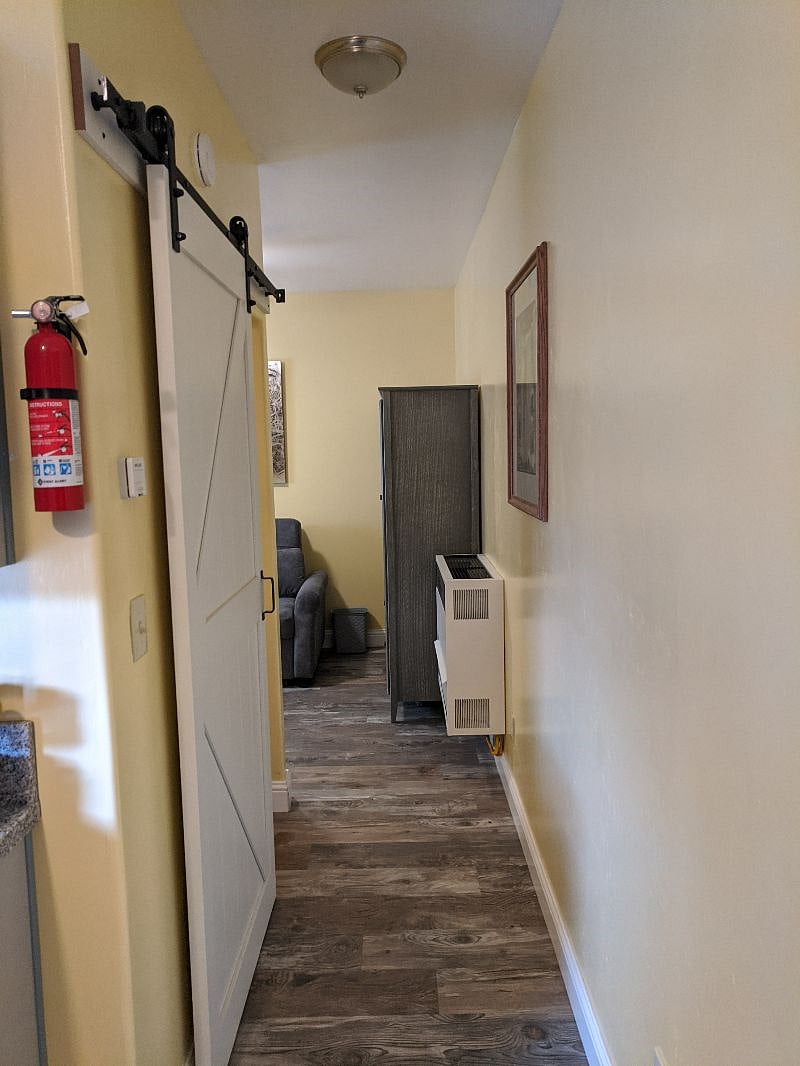 View from kitchen down the hall to the living room / bedroom, with barn door of bathroom seen on the left.