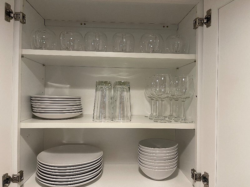 Dishes, glasses, coffee mugs, wine glasses ready in the cabinet.