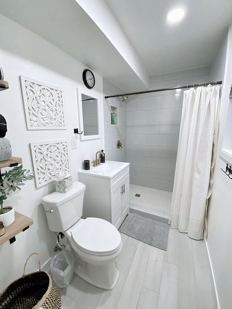 Newly remodeled bathroom with tile shower, vanity, toilet and shelving for towels and toiletries