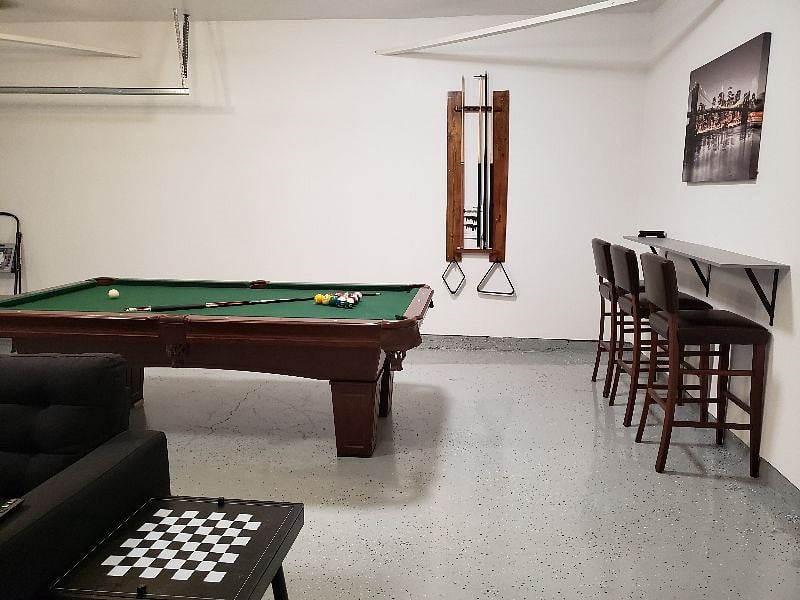 Garage area converted to a Playroom that is will lit with a Pool table, couch and bar area.