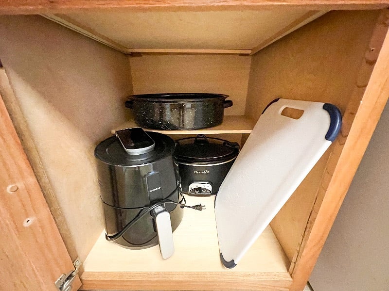 Air fryer, crockpot, & cutting board found in lower cabinet next to refrigerator.