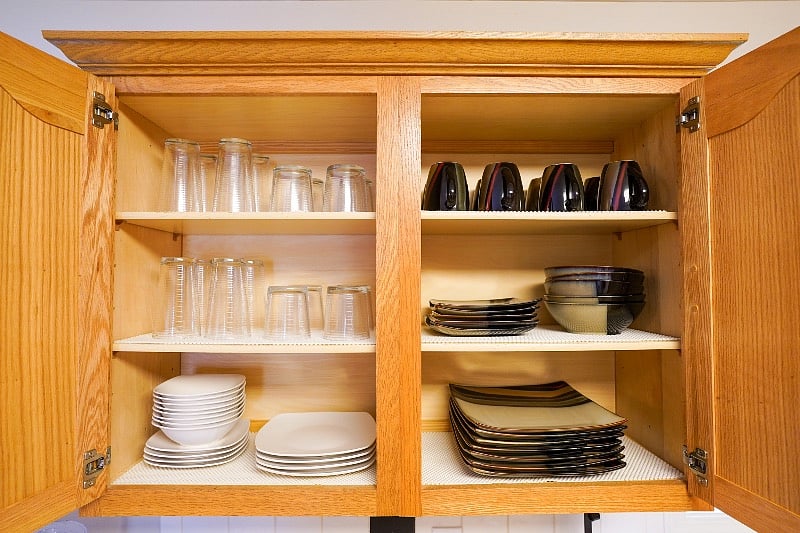 Cups, mugs, dishes, & bowls in upper cabinet next to coffee bar.