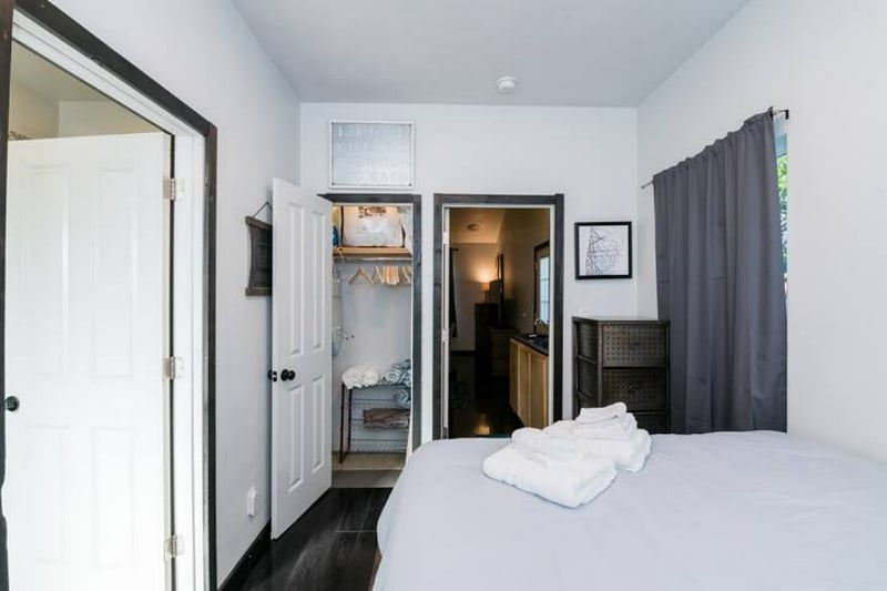 Kitchen leads into bedroom with storage for clothing. Closet with hangers, shoe rack, iron + ironing board.