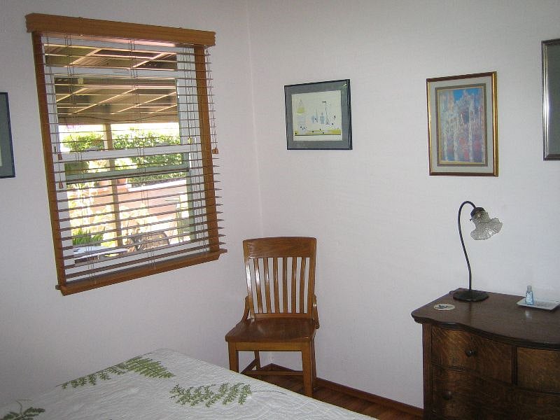 furnished room-to-rent with window facing covered patio, chair, empty dresser with light
