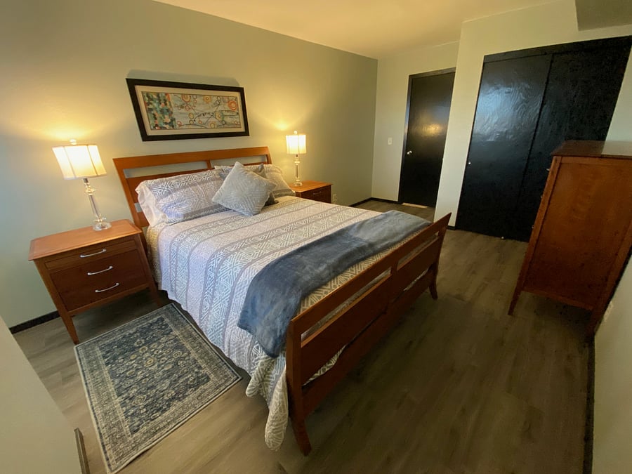 The bedroom features a queen-sized bed with two closets (one with mirrored doors), a chest of drawers, and two nightstands with lamps.