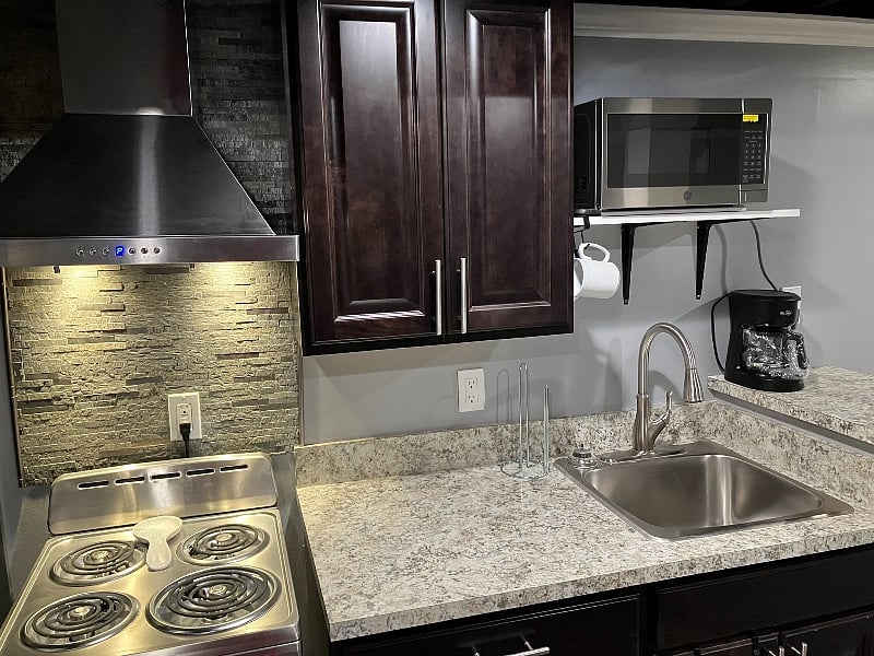 Kitchenette with microwave, refrigerator, exhaust fan, stove, pots, dishes, and utensils.