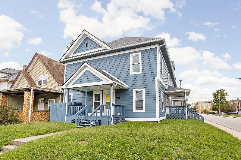 Charming corner view of a renovated blue two-story home with a welcoming front porch, crisp white trim, and spacious wraparound side yard.