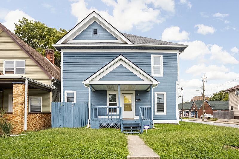 Charming two-story blue home with a welcoming front porch, fenced yard, and a quaint neighborhood setting.