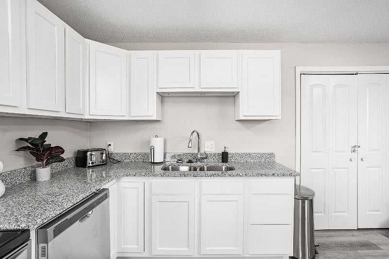 Bright and modern kitchen featuring white cabinetry, granite countertops, and stainless steel appliances, complemented by minimalist decor and a clean, organized layout.