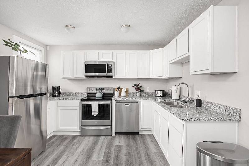 Contemporary kitchen featuring white cabinetry, stainless steel appliances, granite countertops, and sleek wood-look flooring, creating a bright and modern culinary space.