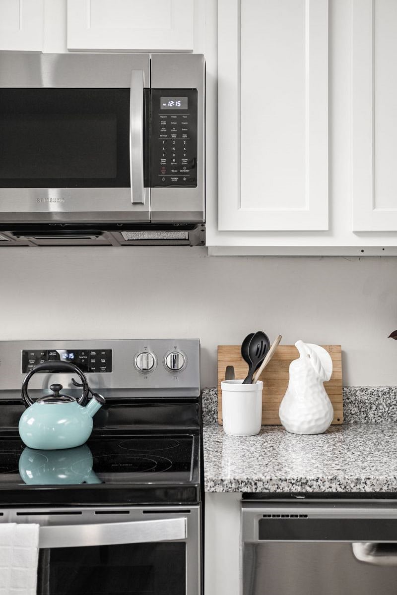 Stylish kitchen countertop scene featuring a modern stainless steel stove, a pastel blue kettle, and neatly arranged cooking essentials including utensils, a cutting board, and a decorative white pitcher.